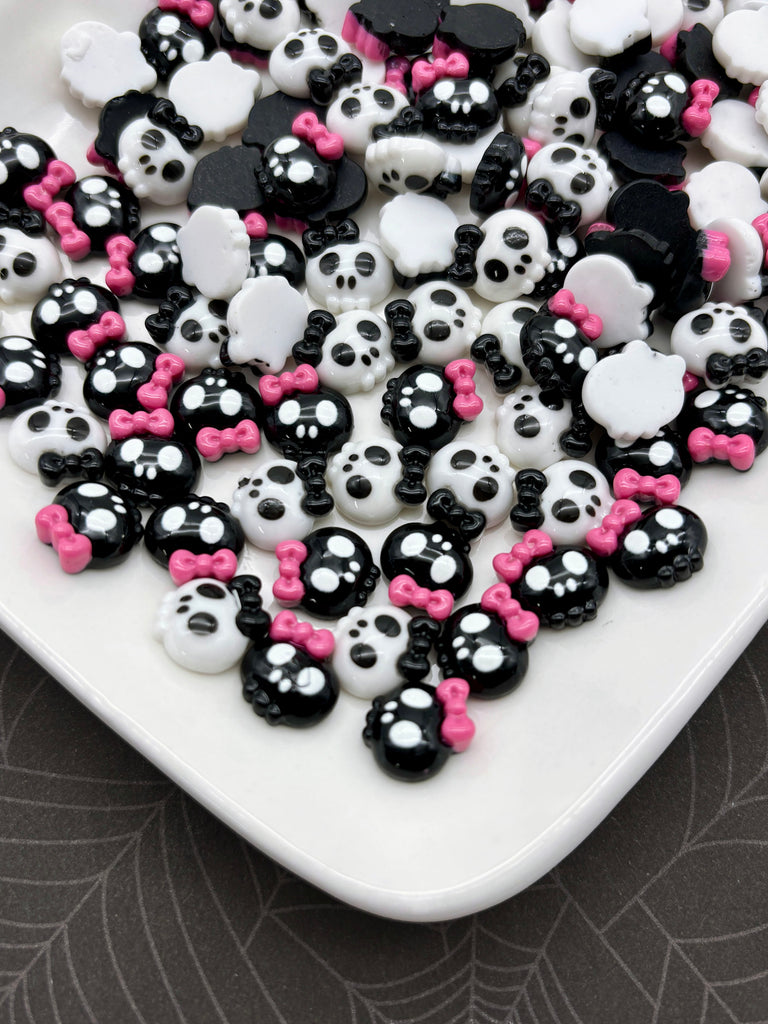 a white plate filled with an assortment of black and white skull-shaped candies, each adorned with a pink bow.