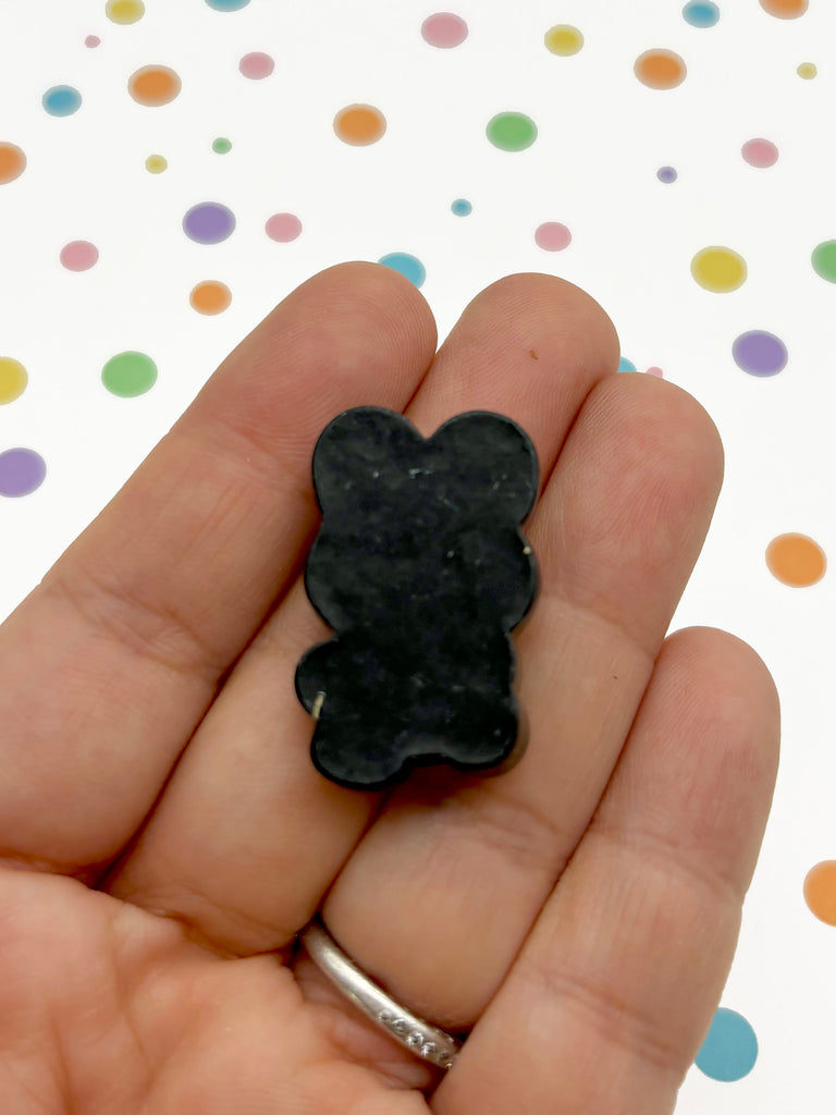 a hand holding a small black teddy bear brooch