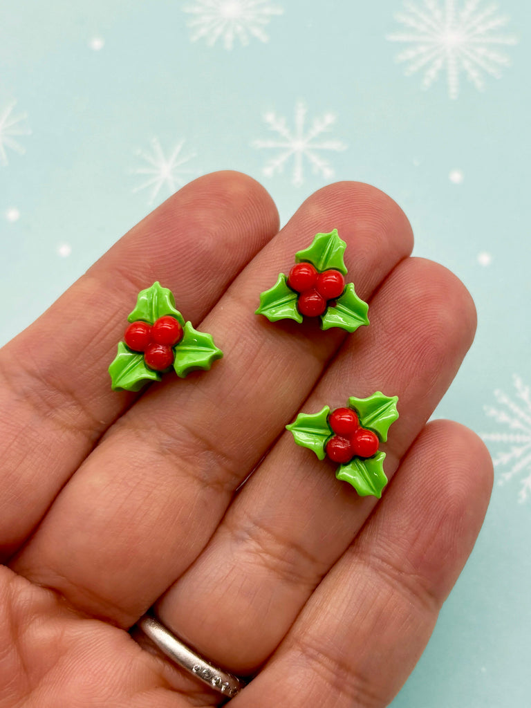 a hand holding three small christmas holly decorations