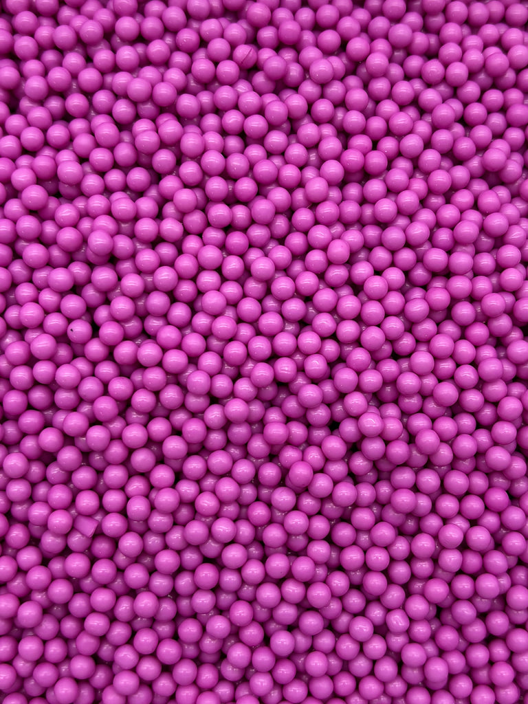 The image is a close-up of numerous small, round, and shiny purple beads or candies.