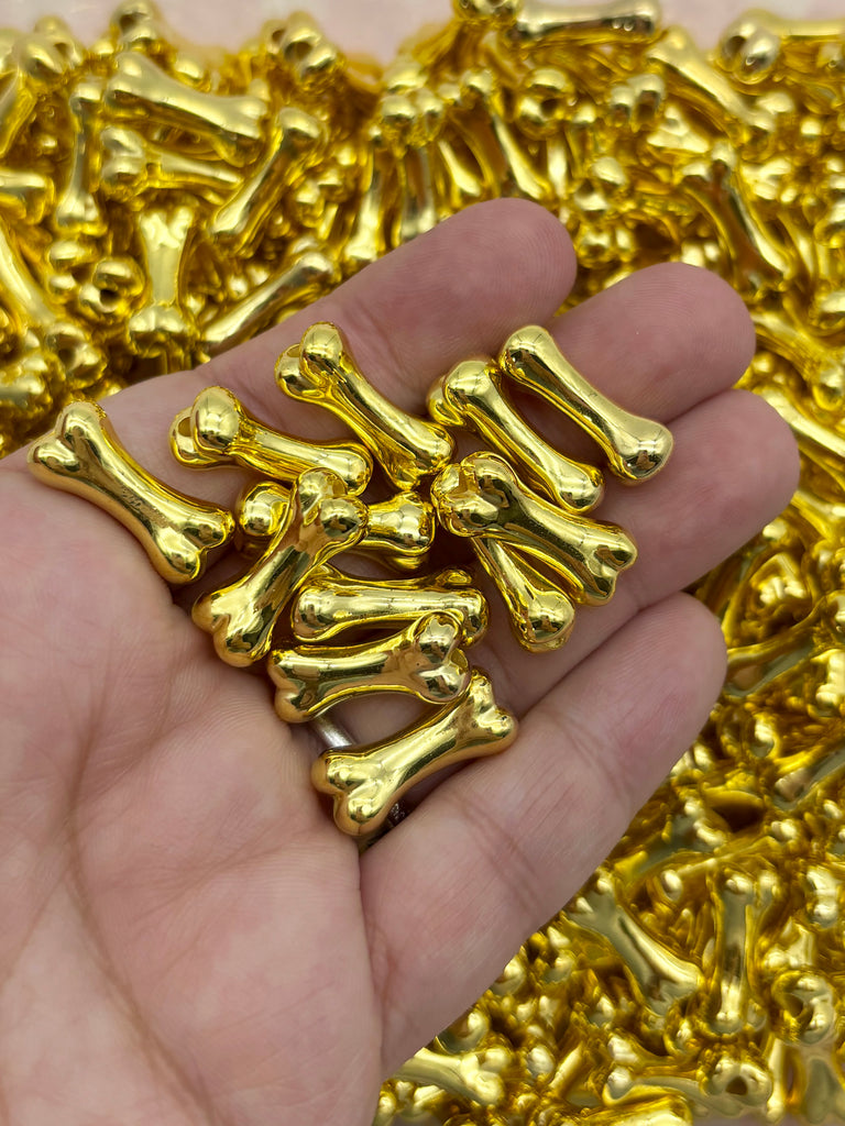 A hand holding a pile of shiny, golden-colored metal objects, possibly beads or small figurines.