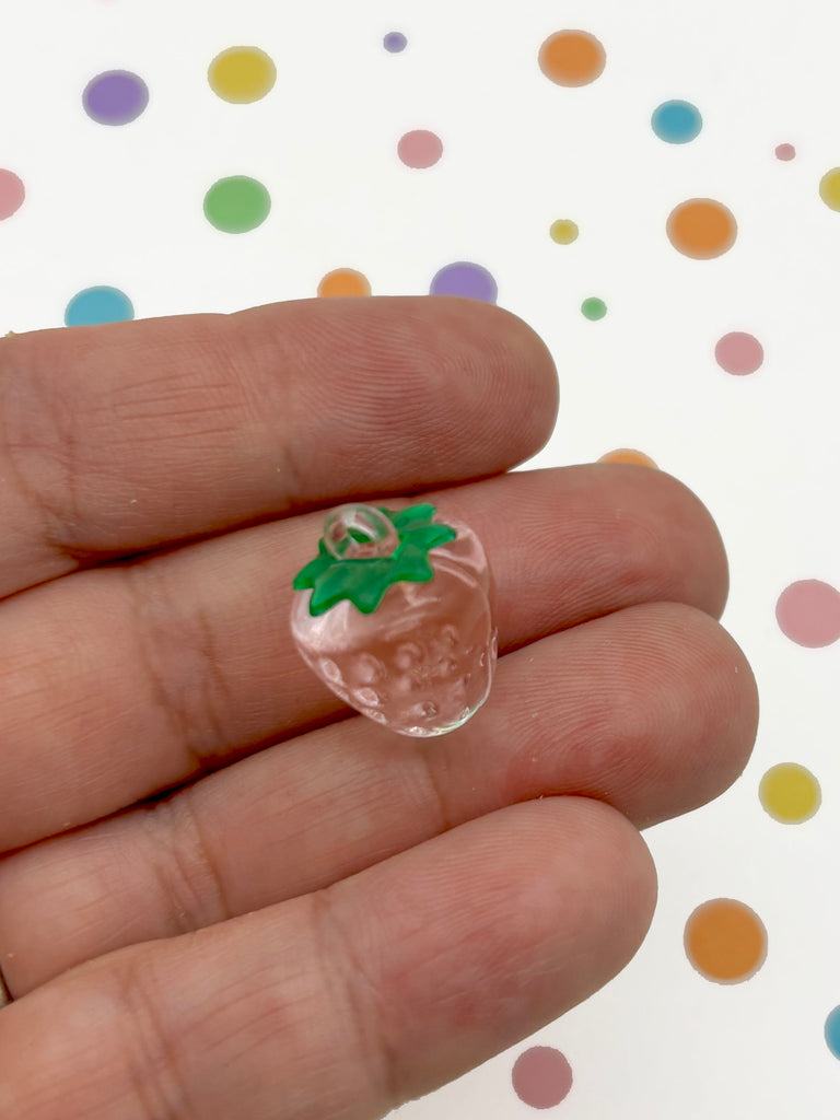 A hand holding a small, clear bead in the shape of a strawberry with a green stem.