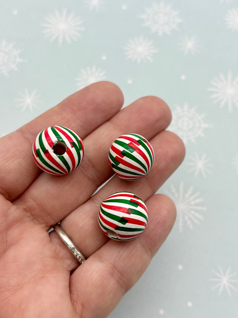 A hand holding three colorful beads with red, green, and white stripes against a snowy background.