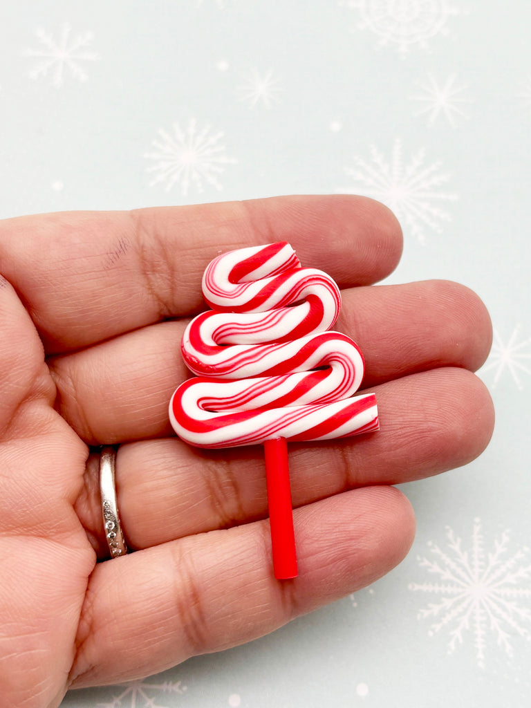 A hand holding a candy cane-shaped ornament against a snowy background.