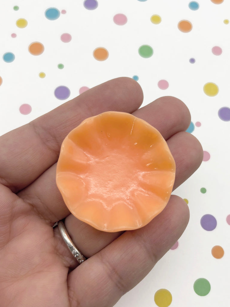 A hand holding a small orange object against a background with colorful polka dots.