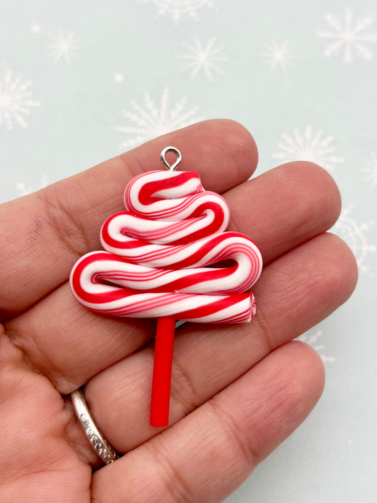 A hand holding a candy cane-shaped pendant against a snowy background.