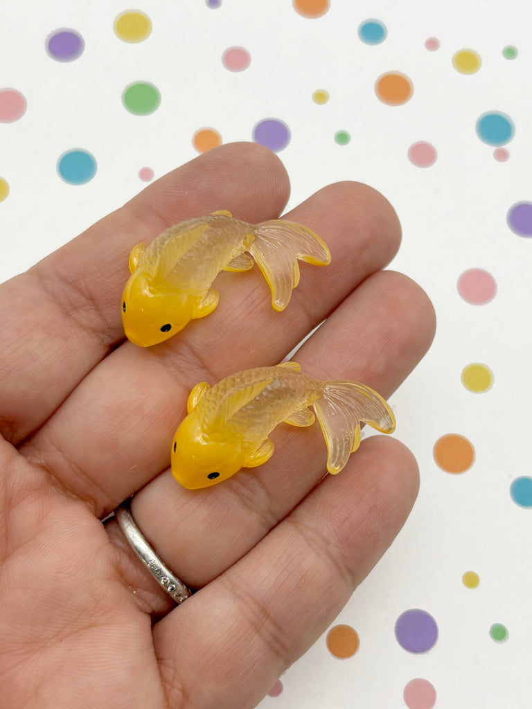 A hand holding two small, yellow fish-shaped objects against a background with colorful polka dots.