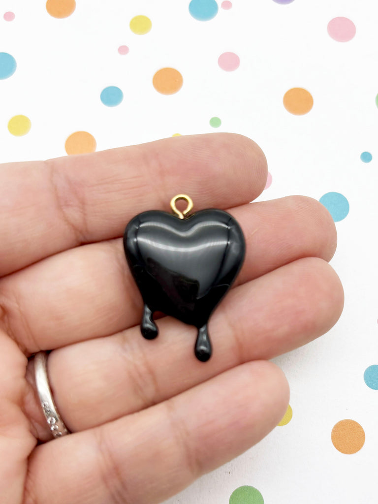 A hand holding a black heart-shaped pendant with a gold-colored clasp.