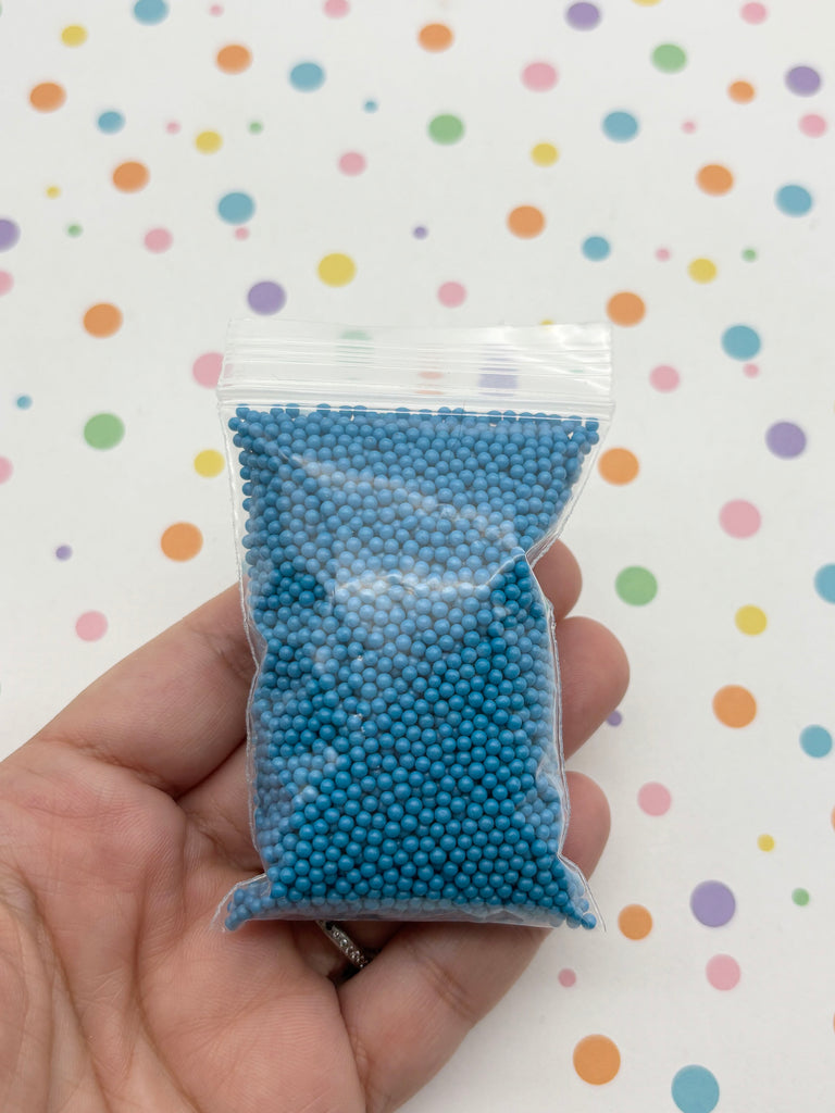A hand is holding a small bag filled with blue beads against a background with colorful polka dots.