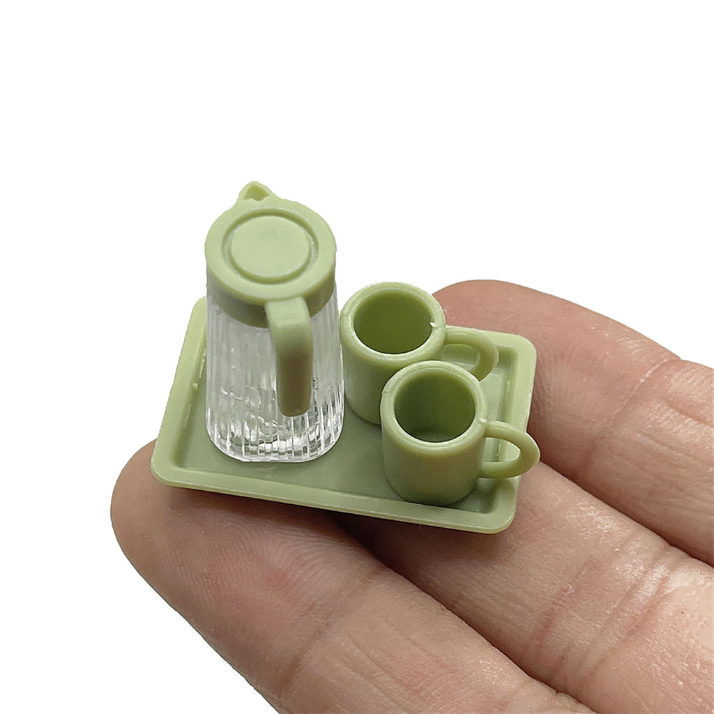 A hand holding a miniature green tray with two matching green cups on it.