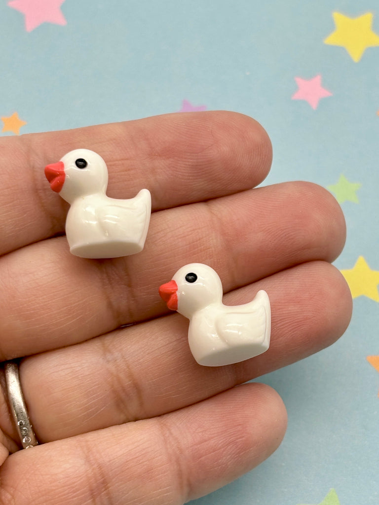 A hand holding two small white duck-shaped charms against a background with colorful stars.