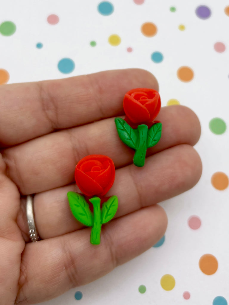 A hand holding two red rose-shaped earrings made of plastic.
