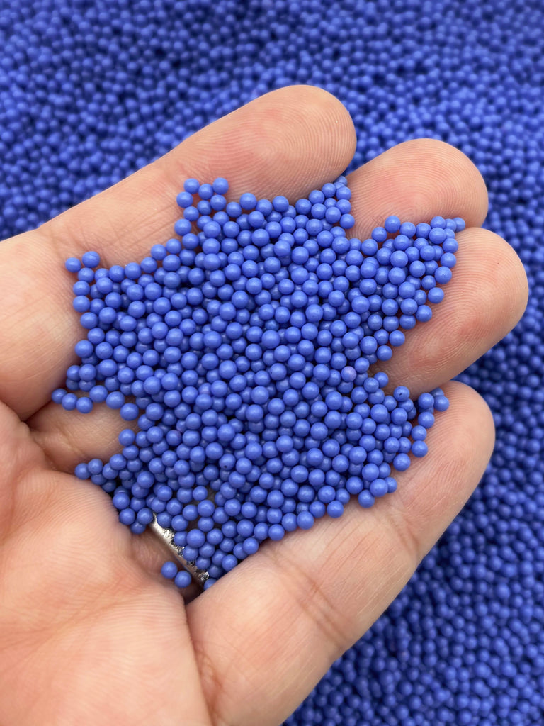 A hand holding a pile of small, round blue beads against a blue background.