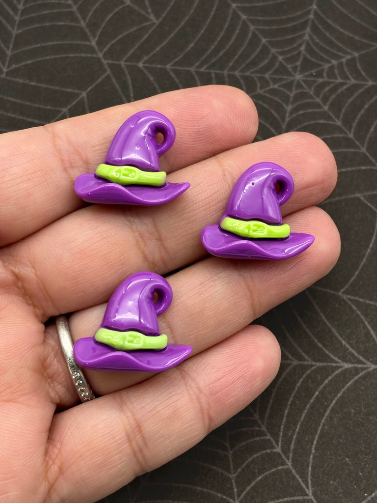 A hand holding three purple and green plastic wizard hats.