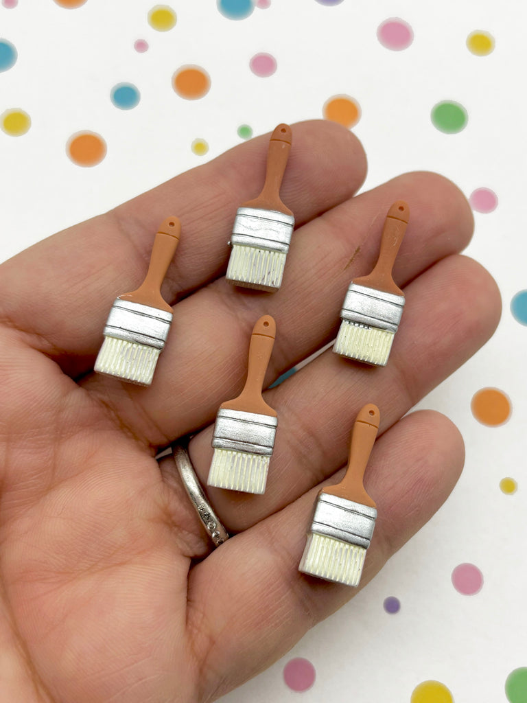 A hand holding five small paintbrush-shaped objects against a background with colorful polka dots.