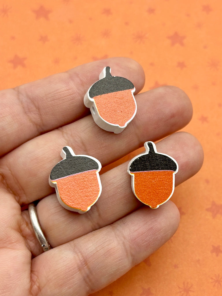 A hand holding three acorn-shaped beads against an orange background with stars.