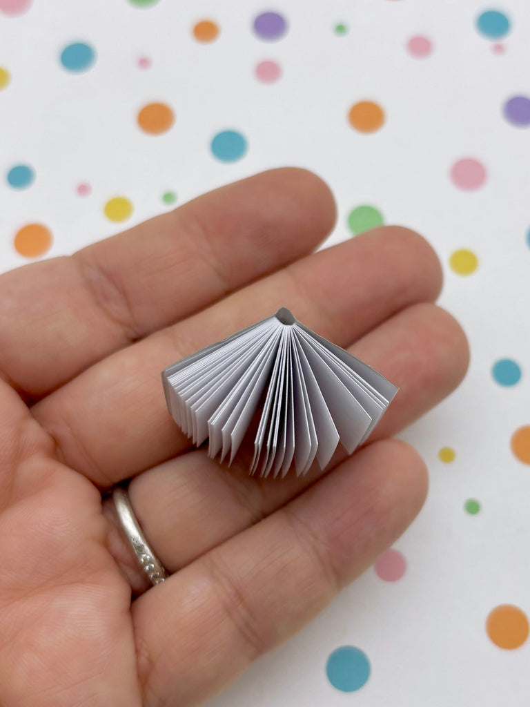 A hand holding a small, open book against a background of colorful polka dots.