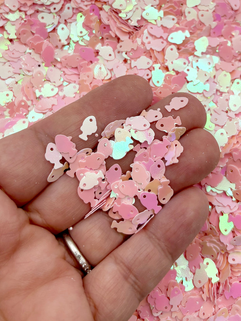 A hand holding a pile of pink and white glittery objects, possibly sequins or confetti.