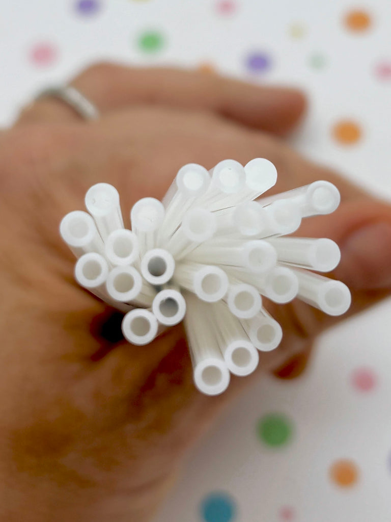 A hand holding a bunch of white straws against a background with colorful polka dots.