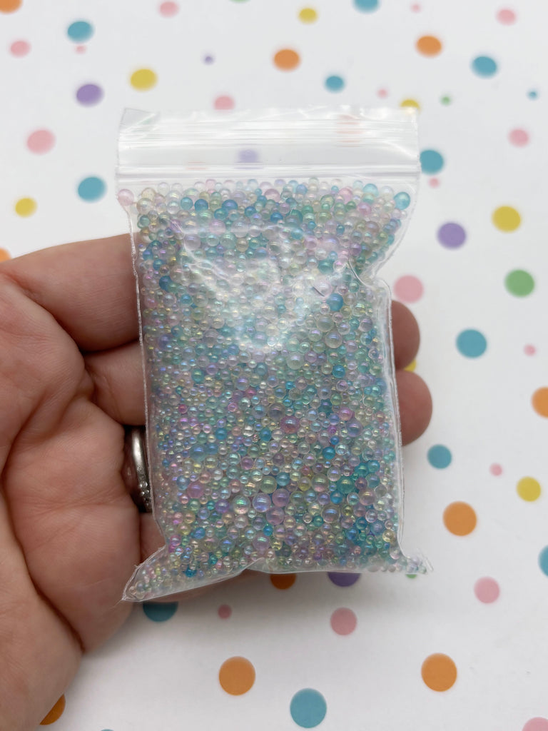 A hand is holding a small bag filled with multicolored beads against a background with colorful polka dots.