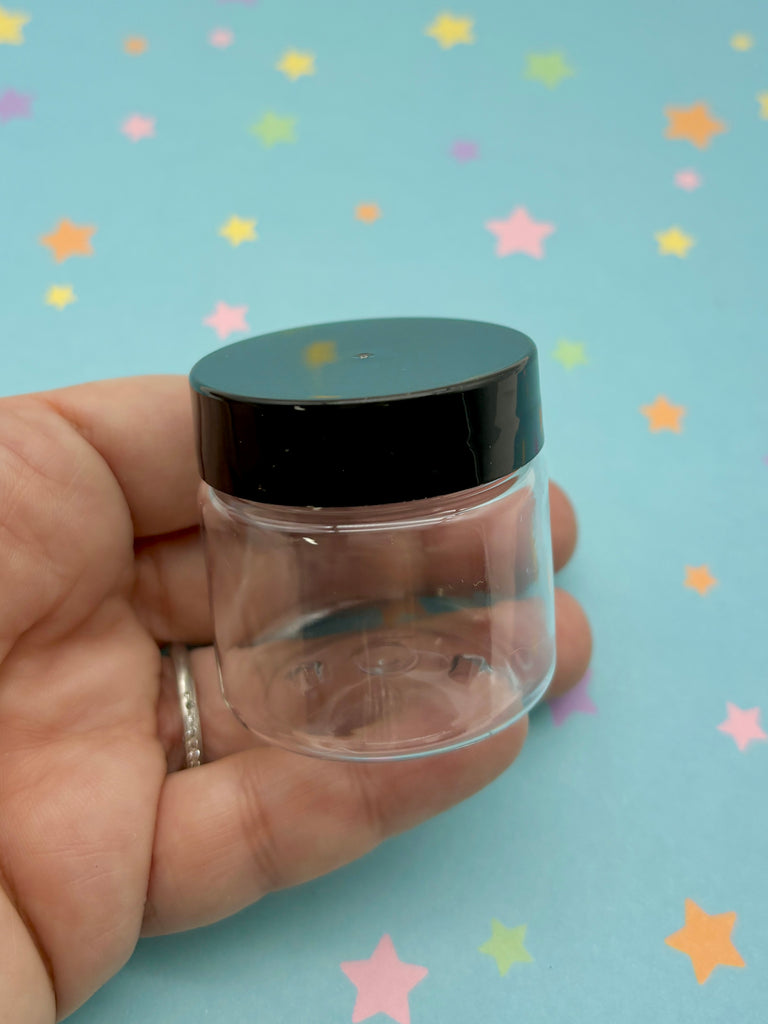 a hand holding a small jar with a black lid