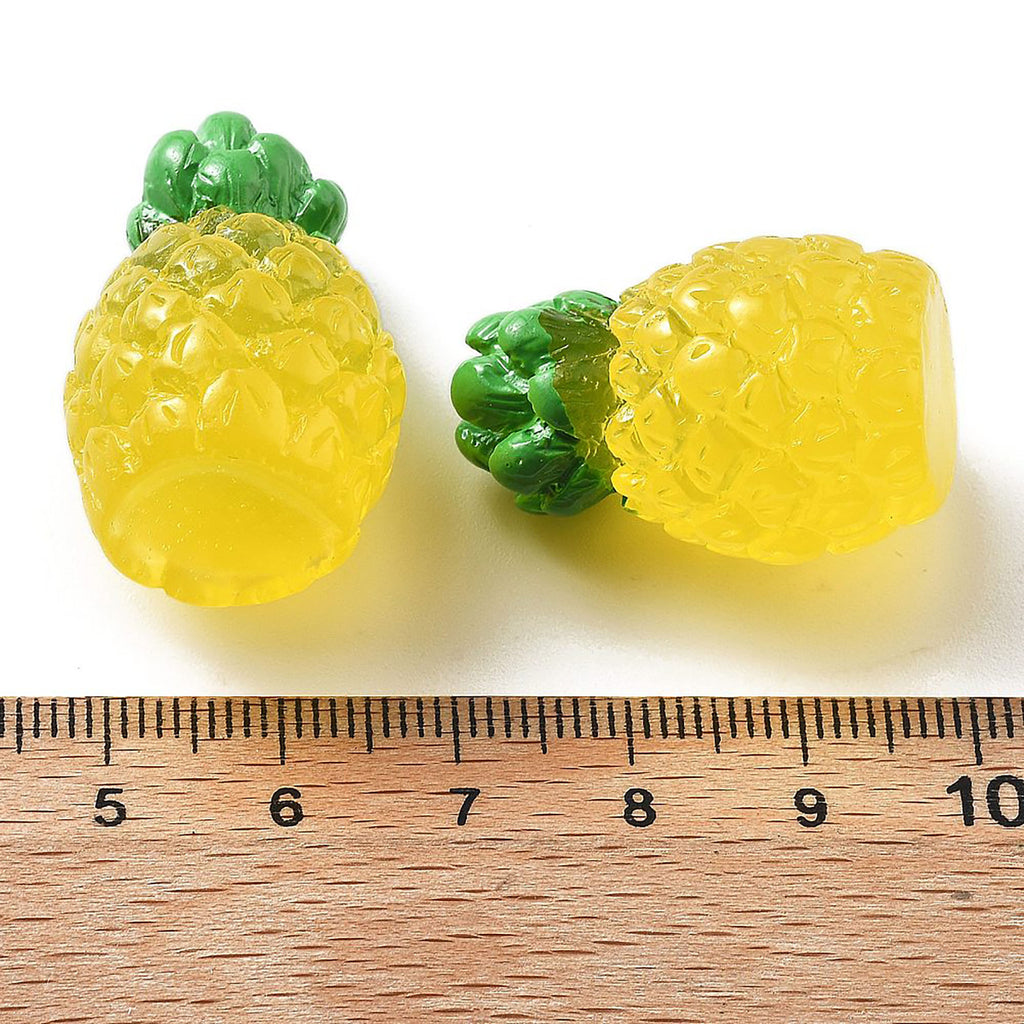 two pineapple-shaped objects, one yellow and one green, placed next to a ruler for size comparison.