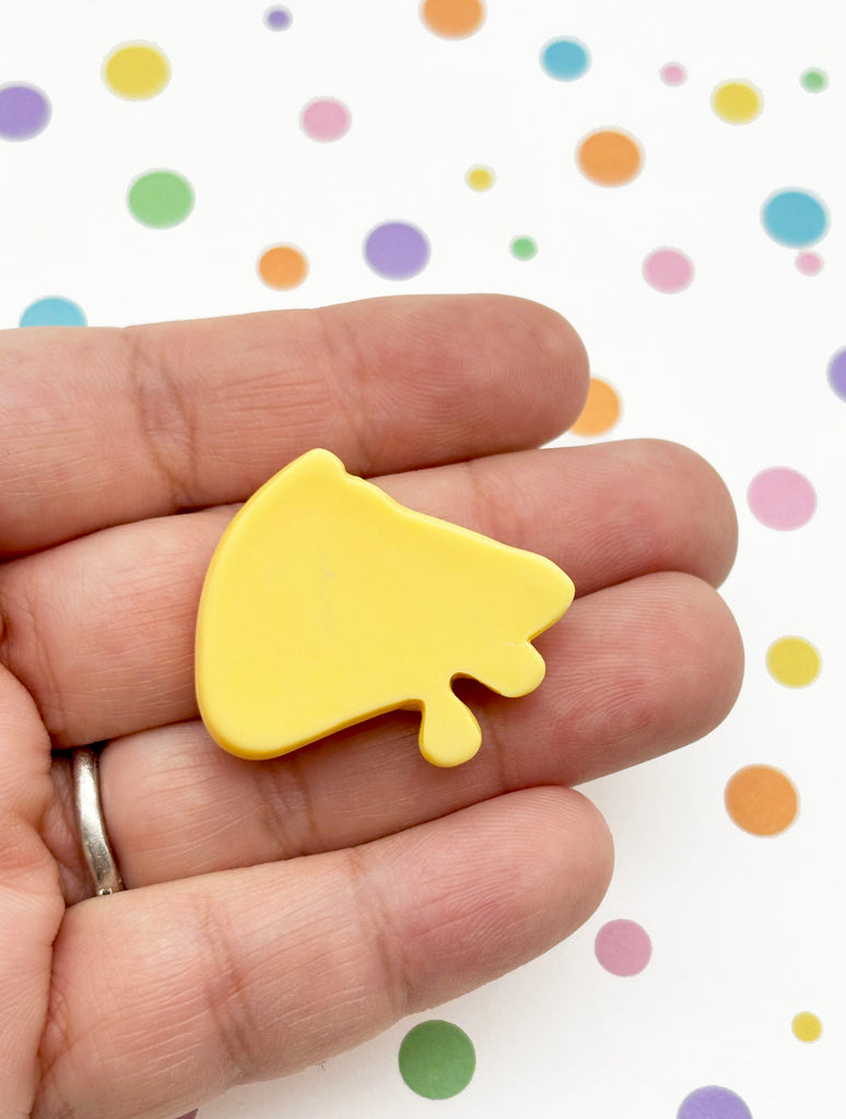 A hand holding a yellow object against a background with colorful polka dots.