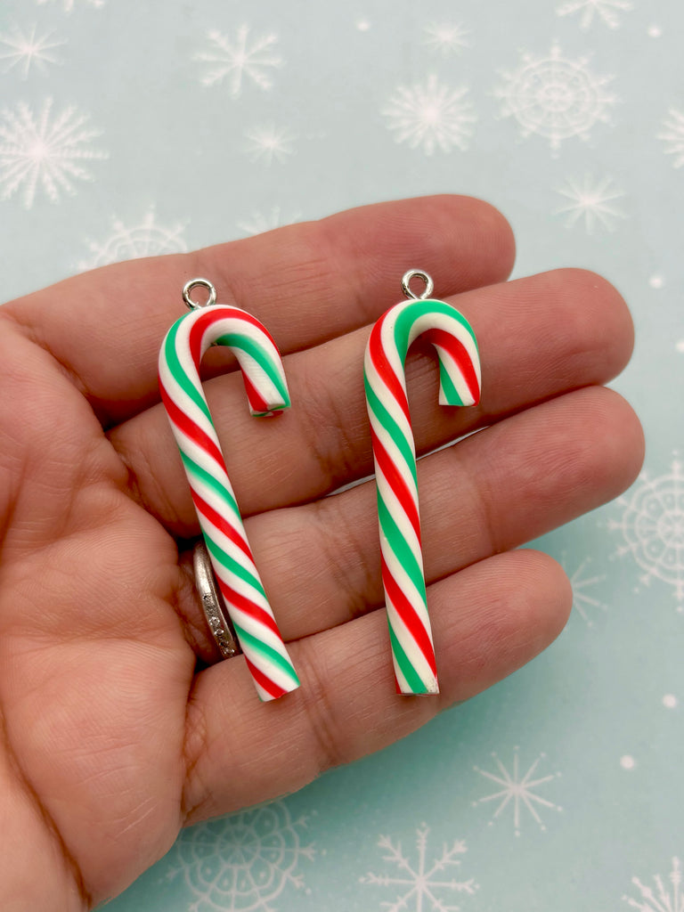 A hand holding two colorful candy cane-shaped charms against a snowy background.