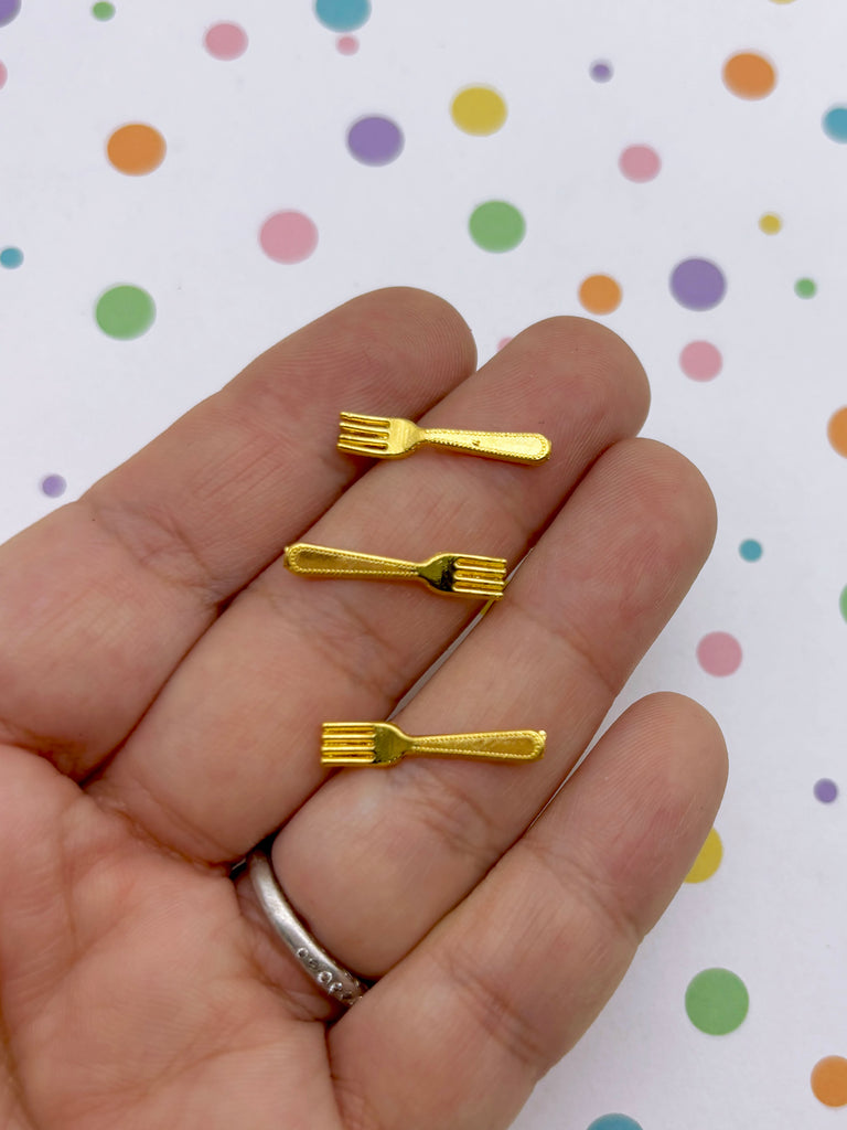 A hand holding three small gold-colored forks against a background with colorful polka dots.