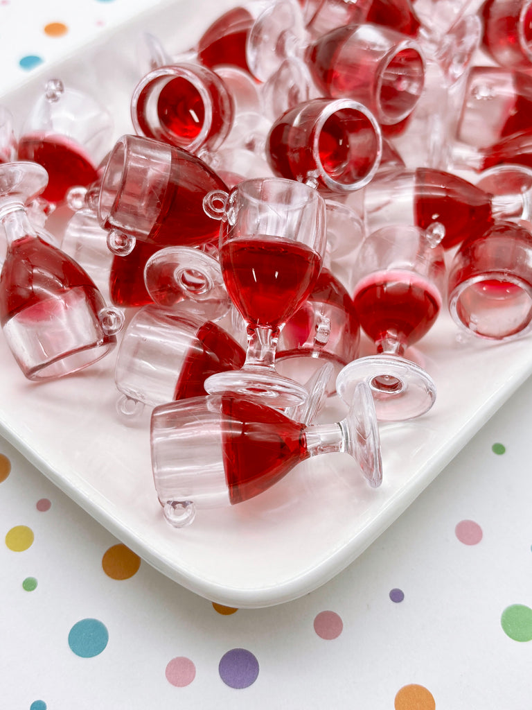 a white plate filled with numerous small, clear plastic wine glasses containing a red liquid, possibly wine or a red-colored beverage. The glasses are arranged in a way that they appear to be spilling out of the plate, creating a visually striking and playful display.
