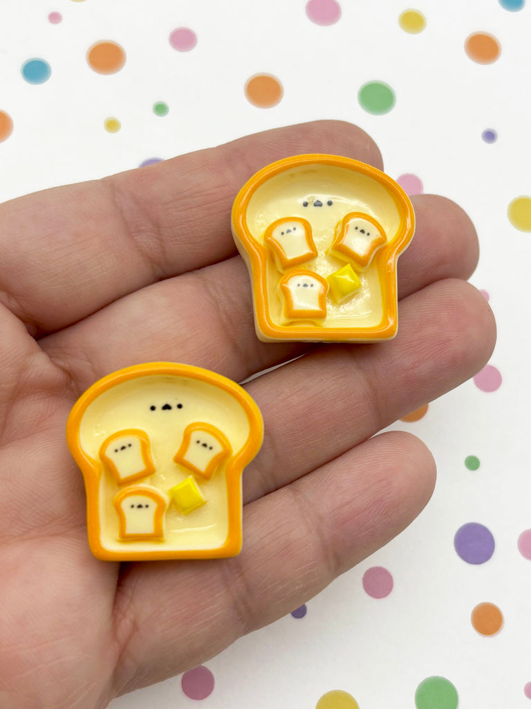 A hand holding two small, orange-colored bread-shaped objects with yellow spots on them, set against a background with colorful polka dots.