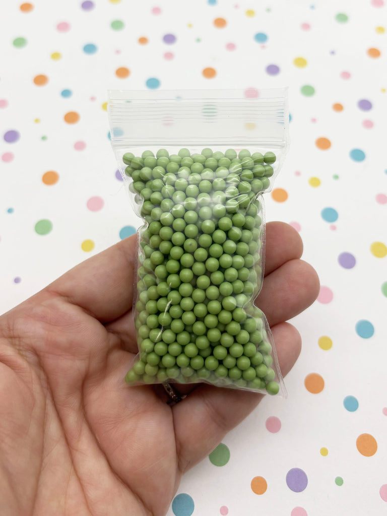 A hand is holding a small bag filled with green beads against a background with colorful polka dots.