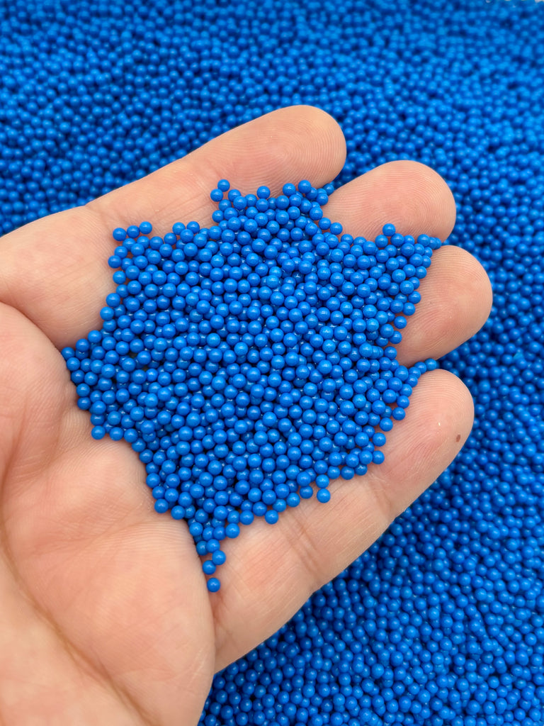 A hand holding a pile of small, round blue beads.