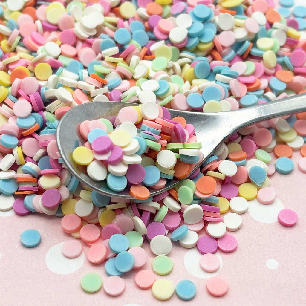 a spoon full of colorful sprinkles on a pink surface