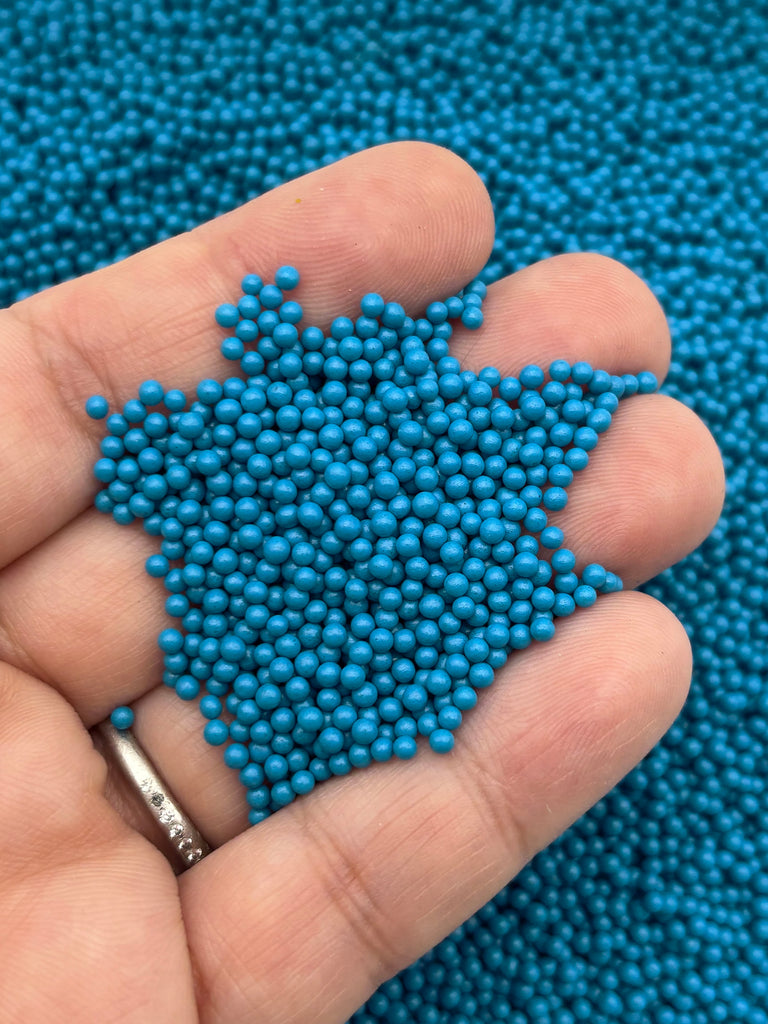 A hand holding a pile of small, blue beads against a blue background.