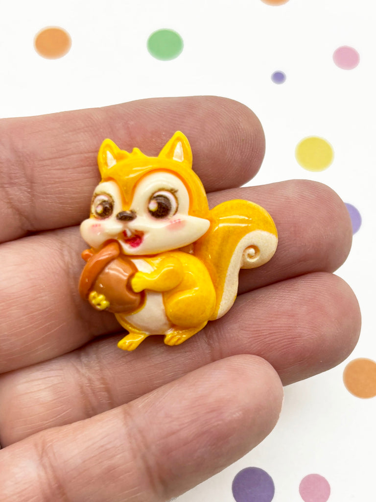A hand holding a small, yellow and white squirrel figurine.
