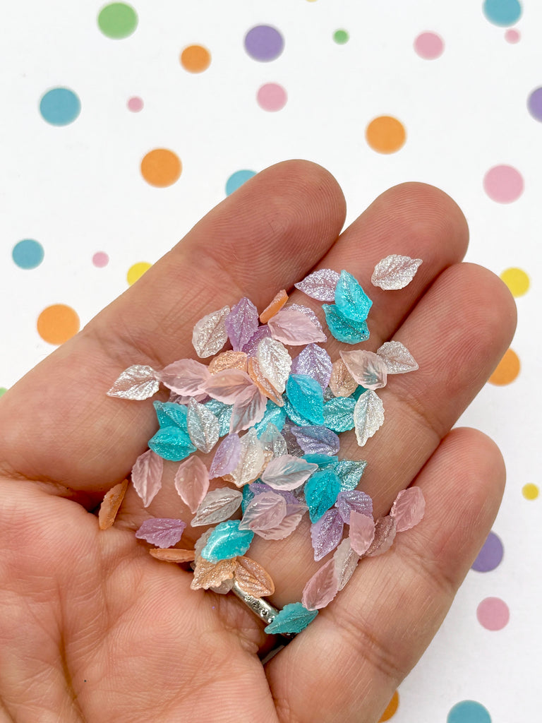 A hand holding a collection of multicolored, glittery, and shiny objects resembling leaves or small decorative pieces.