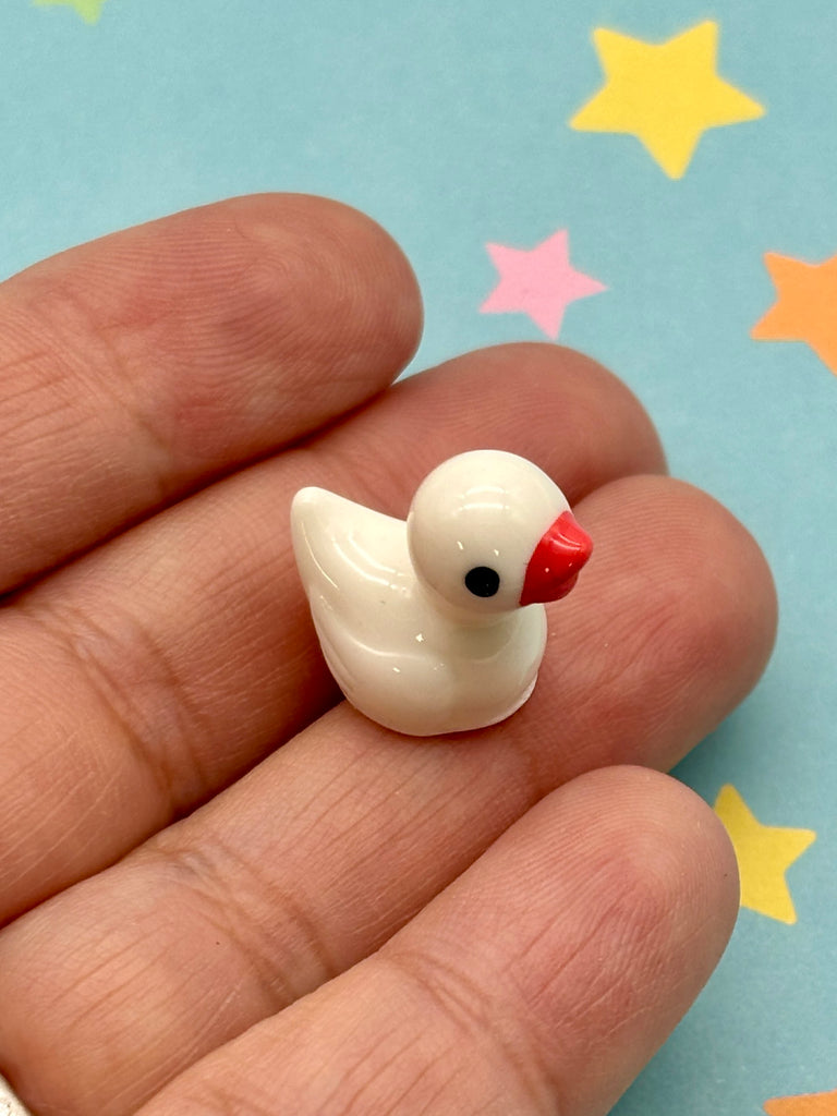 A small white ceramic duck figurine is being held in a person's hand against a background of colorful stars.