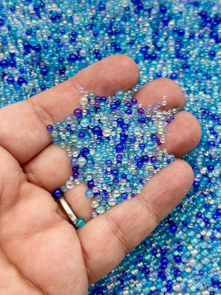 A hand holding a collection of small, colorful beads in various shades of blue and white against a background of similar colored beads.