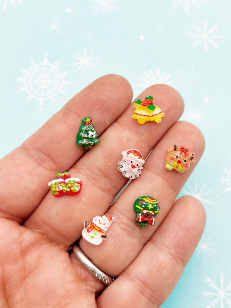 A hand holding a collection of small, colorful Christmas-themed stickers on fingers against a blue background with white snowflakes.