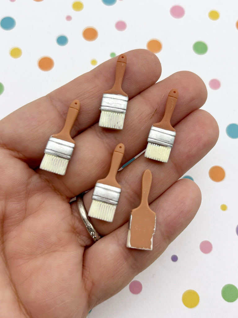 A hand holding five small paintbrush-shaped objects against a background with colorful polka dots.