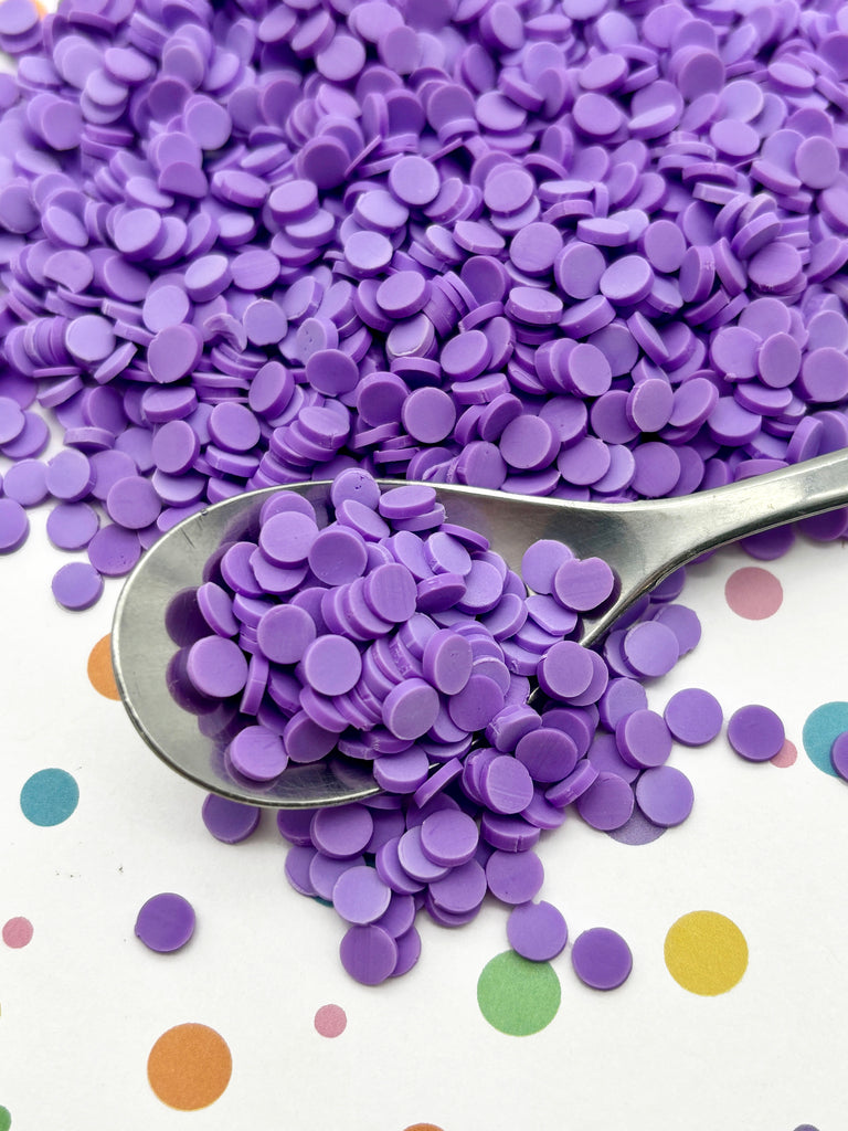 a spoon filled with purple confetti on top of a table