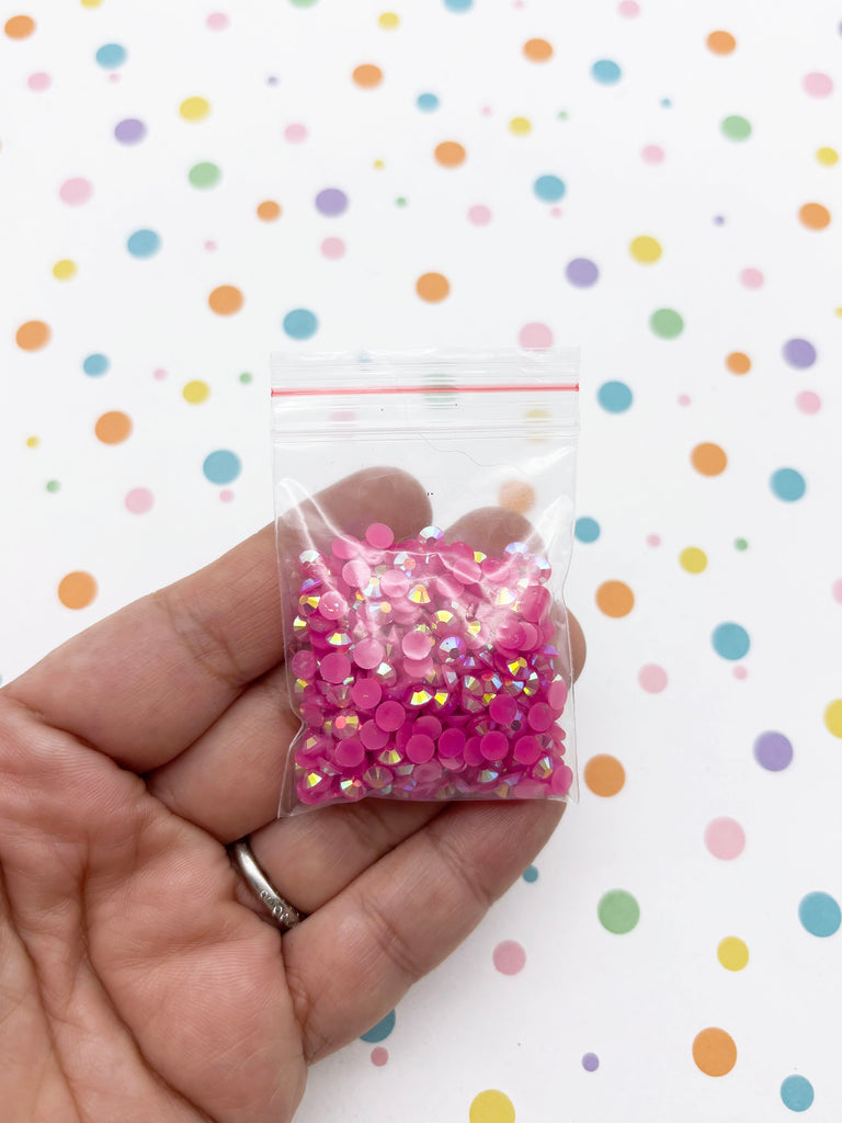 A hand holding a small bag filled with pink and silver glittery beads against a background of colorful polka dots.