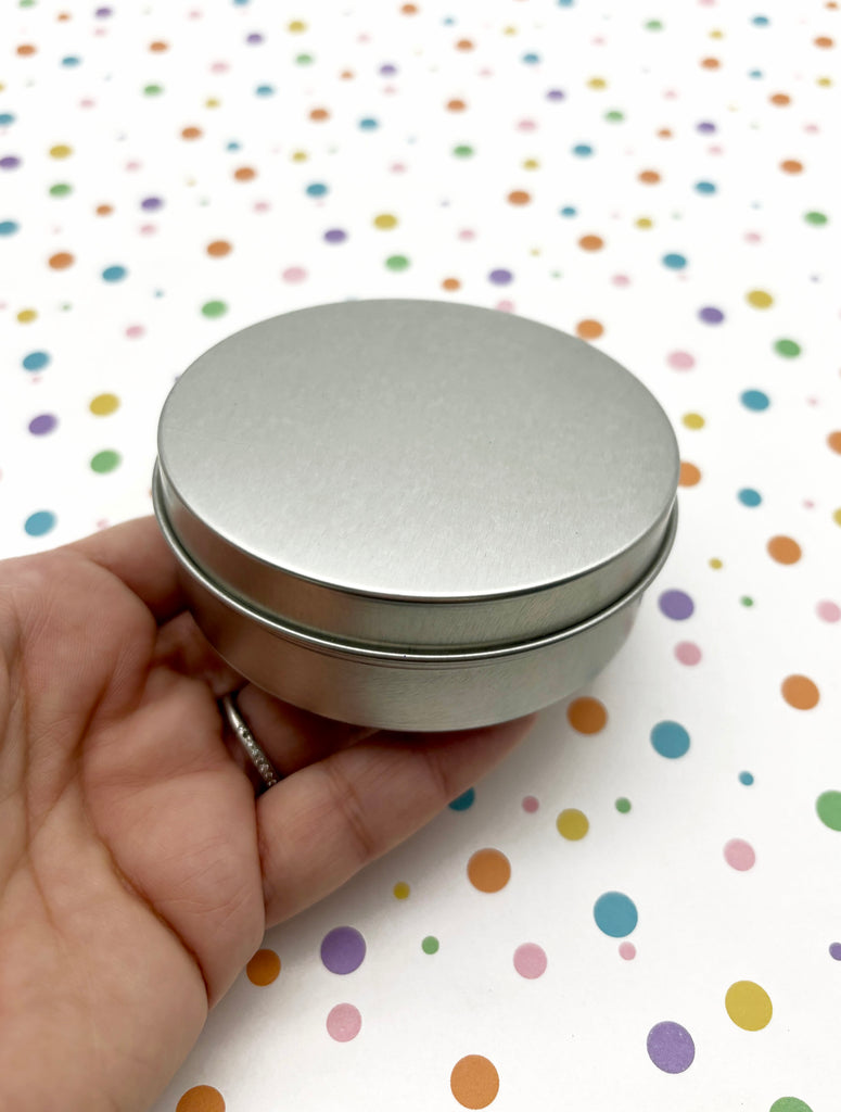 a hand holding a small round metal container