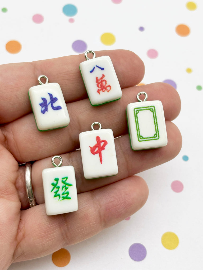A hand holding a collection of colorful pendants featuring various designs, including symbols and patterns.