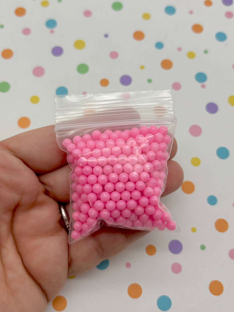 A hand is holding a small bag filled with pink beads against a background with colorful polka dots.