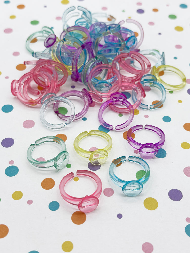 A pile of colorful plastic rings, including clear, purple, and pink rings, scattered on a white background with polka dots.