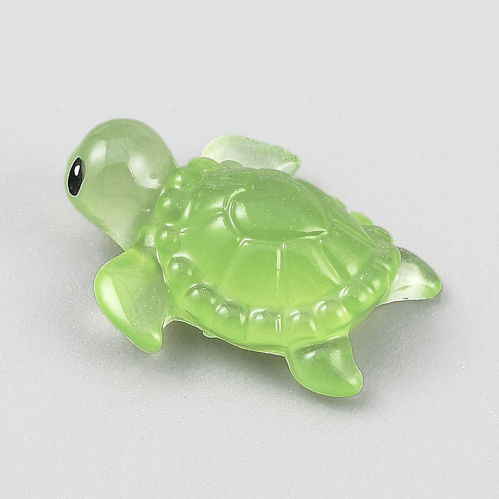 A small, green turtle figurine is sitting on a white surface.