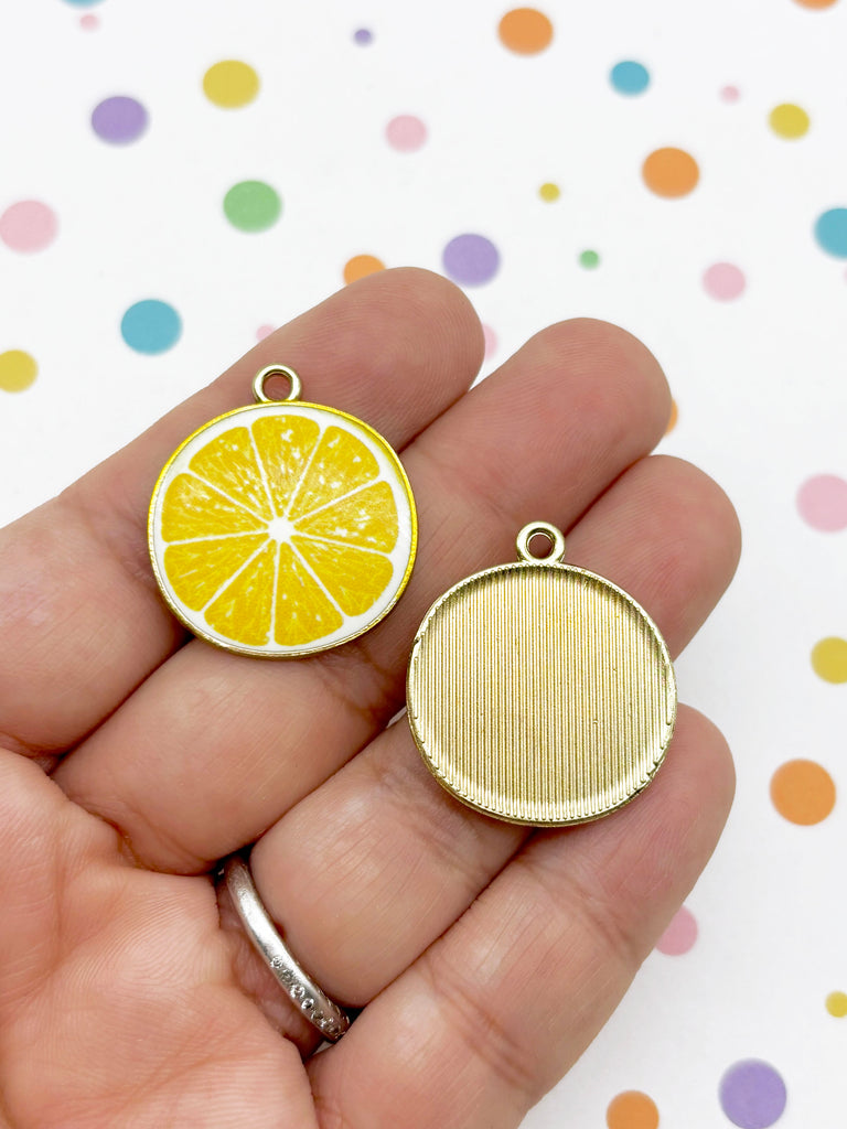 A hand holding two charms, one depicting a slice of lemon and the other a plain round object.