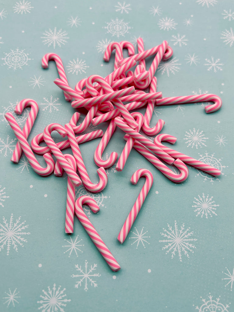 A pile of pink and white striped candy canes is scattered on a blue background with white snowflakes.